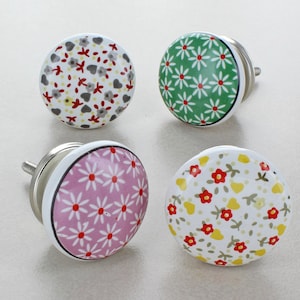 May include: Four ceramic cabinet knobs with floral patterns. The knobs are white with different coloured floral designs. The knobs have a silver metal screw on the back.