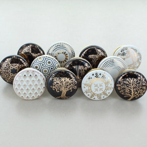 May include: A set of 11 black and white ceramic knobs with gold accents. The knobs feature various geometric and floral designs.