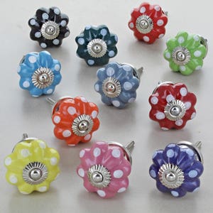 Könnte beinhalten: Sortiment von 10 Keramik-Schubladengriffen in Blumenform mit weißen Punkten. Die Griffe sind in verschiedenen Farben, darunter Rot, Blau, Grün, Gelb, Rosa und Schwarz.