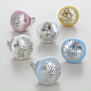 May include: Six ceramic cabinet knobs with a silver filigree design. The knobs are in various colors, including pink, white, yellow, and blue.