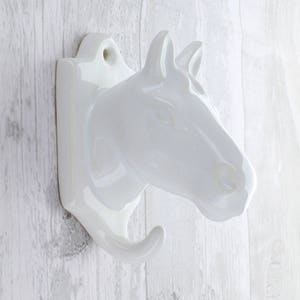 May include: White ceramic horse head wall hook. The hook is shaped like a horse's head with a single hook protruding from the bottom.