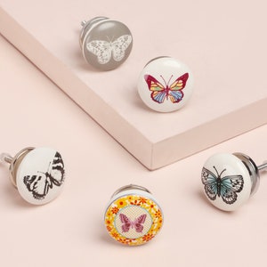 May include: Set of five ceramic drawer knobs featuring butterfly designs. The knobs are round and have a silver screw. The butterflies are in various colours and patterns, including black and white, blue and white, yellow and red, and pink and yellow.