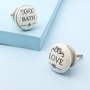 May include: Two white ceramic knobs with silver metal stems. One knob says "BATH" and the other says "LOVE".
