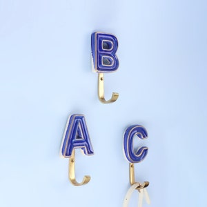 Ganchos de pared con letras de latón con acabado antiguo y cerámica pintada a mano con monograma personalizado de G Decor, hechos a mano, en azul real, esmaltado craquelado.