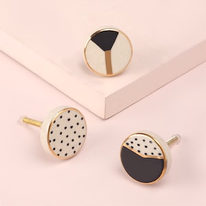 Peut inclure: Trois boutons de porte en céramique avec une bordure dorée. Un bouton a un motif de pois noir et blanc, un autre a un motif géométrique noir et blanc et le dernier a un motif de demi-cercle noir et blanc.