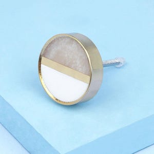 May include: A round, white and beige marble cabinet knob with a gold trim and a silver screw.