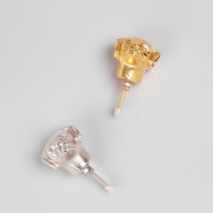 Op de afbeelding: Twee decoratieve kastknoppen in de vorm van een hondenhoofd, één goudkleurig en één zilverkleurig. Elke knop heeft een schroefdraad voor bevestiging. De knoppen zijn waarschijnlijk van metaal en ontworpen voor meubels.