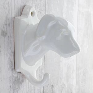 May include: White ceramic dog head coat hook. The hook is shaped like a dog's head with a curved hook for hanging items.