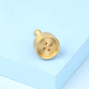 May include: A gold-toned button-shaped cabinet knob with five holes in the centre.