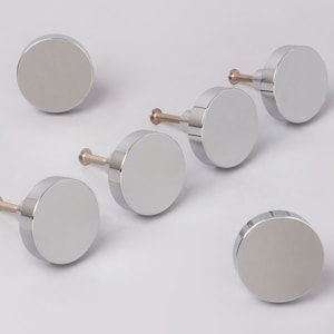 Op de afbeelding: Zes ronde, zilverkleurige kastknoppen met een gladde, glanzende afwerking. Elke knop heeft een kleine schroef om aan een kastdeur te bevestigen.