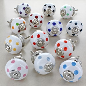 Może przedstawiać: Zestaw 12 ceramicznych gałek do szafek z białą podstawą i kolorowymi kropkami. Gałki mają srebrną metalową podstawę i srebrny metalowy guzik.