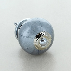 Op de afbeelding: Decoratieve kastknop met een grijze, gemarmerde afwerking. De ronde knop heeft een zilverkleurige basis en een decoratieve, geschulpte rand. Ontworpen voor eenvoudige installatie op meubels. Diameter ca. 4 cm.