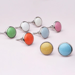May include: A selection of ceramic cabinet knobs in various colours with a crackle glaze. The knobs are in green, white, orange, blue, pink, yellow, and light blue, each with a silver metal base and a crackle pattern.