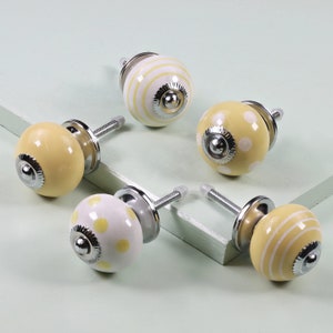 May include: Five ceramic knobs with yellow and white patterns. The knobs have a chrome finish and are designed for use on cabinets or drawers.