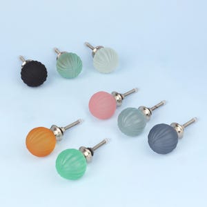 Può includere: Una collezione di pomelli decorativi colorati per mobili. I pomelli sono rotondi con un design a coste e sono disponibili in vari colori, tra cui nero, verde, rosa, arancione e grigio. Ogni pomello ha una vite color argento.