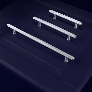 May include: Four silver cabinet pulls with a textured, diamond-patterned design. The pulls are mounted on a dark blue cabinet door. The pulls have a cylindrical bar and are mounted on two small, rounded feet.