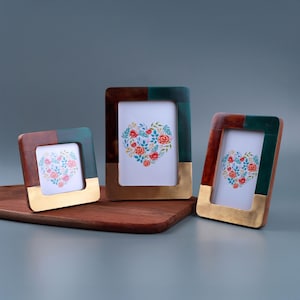 May include: Three decorative picture frames with a heart-shaped floral design. The frames have a mix of colours, including brown, green, and gold. The frames are displayed on a wooden surface.