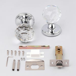 May include: A set of two crystal door knobs with a faceted design, mounted on a shiny chrome base. The hardware set includes a latch, strike plate, screws, and other installation components. The door hardware is designed for interior doors.