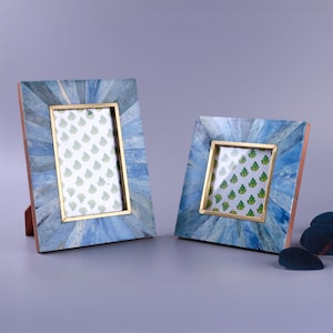 May include: Two decorative picture frames with blue and gold detailing. The frames feature a mosaic design in shades of blue and a gold border around the picture area. The frames are upright, displaying a patterned image.
