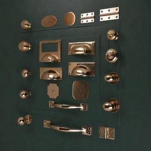 May include: A collection of polished brass hardware including various round knobs, cup pulls, rectangular backplates, and hinges. The assortment features smooth and ribbed textures, arranged on a dark green surface to display the metallic finish.