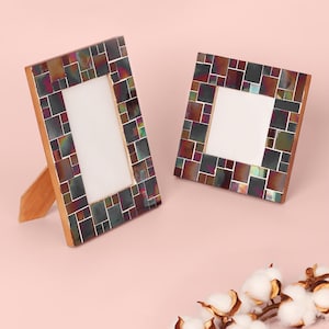 May include: Two decorative photo frames with iridescent mosaic tile borders. The frames have a wooden backing and stand. One frame is rectangular, and the other is square. The frames are on a light pink background.