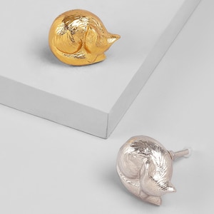 May include: Two decorative cabinet knobs in the shape of a sleeping cat. One knob is gold-colored, and the other is silver-colored. The knobs are made of metal and have a detailed design.