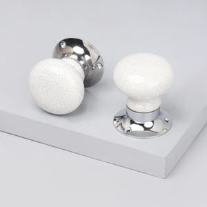 May include: Two door knobs with a white, crackled ceramic finish and shiny chrome bases. The knobs have a rounded shape and are designed for easy gripping. The hardware is set against a neutral background.