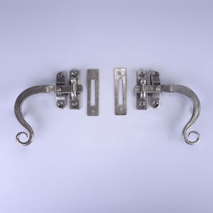 Peut inclure: Ensemble de deux loquets de fenêtre de couleur argentée, de style ancien. Chaque loquet comprend une poignée incurvée avec une extrémité enroulée, une plaque rectangulaire et une gâche assortie. La quincaillerie est conçue pour une esthétique classique ou vintage.