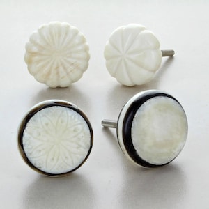 Può includere: Quattro pomelli decorativi per armadi. Due sono bianchi con disegni floreali intagliati e due sono bianchi con accenti neri e marroni. I pomelli hanno una forma rotonda e sono realizzati in un materiale lucido. I pomelli hanno una vite argentata per l'installazione.