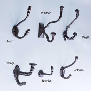 Puede incluir: Colección de seis ganchos de pared decorativos de metal en varios estilos, incluyendo "Acorn", "Windsor", "Regal", "Heritage", "Beehive" y "Victorian". Cada gancho es de color oscuro, con diseños únicos y placas de montaje. Los nombres de los ganchos están impresos debajo.