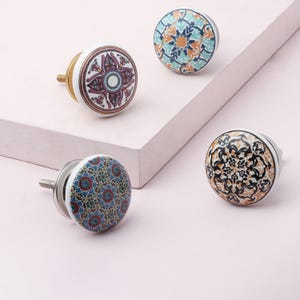 May include: Four decorative ceramic cabinet knobs with various colorful patterns. The knobs have white bases and metal hardware. Designs include floral and geometric patterns in shades of blue, orange, black, and purple.