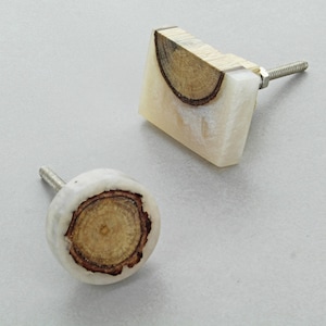 Peut inclure: Deux boutons de meuble décoratifs. L'un est carré, l'autre est rond. Les deux ont une base en résine de couleur claire avec une section de grain de bois. Le bouton carré a un dessus en bois. Chaque bouton a une vis argentée pour l'installation.