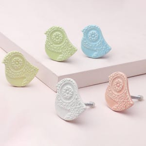 May include: A selection of pastel-coloured bird-shaped cabinet knobs. The knobs are light green, light blue, white, and pink. Each knob features a detailed, embossed design and a silver screw for fitting.