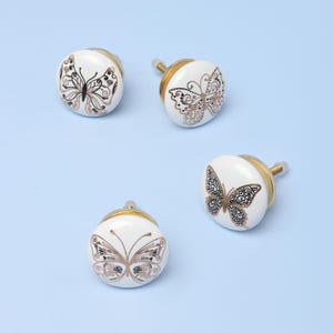 May include: Four white ceramic cabinet knobs with gold accents and black butterfly designs.