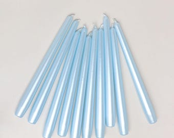 May include: A collection of ten slender, tapered candles in a light, metallic baby blue finish. Each candle features a smooth, cylindrical body with a pointed top and a flat base, arranged in a fan-like formation against a neutral background.