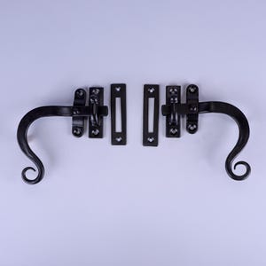 May include: Black wrought iron window or cabinet hardware set. The set includes two curved handles with a scroll design and two sets of latches. The hardware is designed for a traditional or rustic aesthetic.