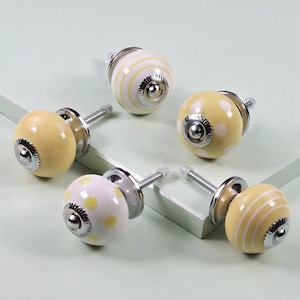 May include: Six decorative cabinet knobs with a mix of patterns. The knobs are primarily yellow and white, with designs including stripes and polka dots. Each knob has a silver-colored base and screw.