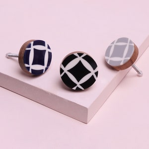 Op de afbeelding: Drie ronde houten knoppen met een wit geometrisch ontwerp op een blauwe, zwarte en grijze achtergrond.