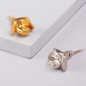 Op de afbeelding: Twee decoratieve kastknoppen in de vorm van hondenkoppen, één goudkleurig en één zilverkleurig. Elke knop heeft een schroefdraad voor bevestiging. Deze decoratieve knoppen zijn ideaal om een unieke touch aan meubels toe te voegen.