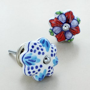 May include: Two ceramic flower-shaped drawer knobs with a white background and blue and red floral designs. The knobs have a silver screw.