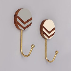 May include: Two decorative wall hooks. Each hook features a wooden, circular base with a painted chevron design in gray and brown, and cream and brown. The hooks are gold-colored metal.