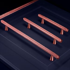 May include: Copper-colored cabinet pulls with a textured, dotted pattern. The pulls are cylindrical with conical supports, arranged on a dark blue surface. The hardware is designed for furniture and home decor.