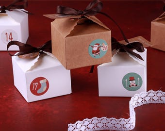 May include: Advent calendar boxes in white and brown, adorned with brown ribbons. Each box features a numbered sticker with festive illustrations, including a Santa Claus and a snowman. A white lace ribbon is visible.