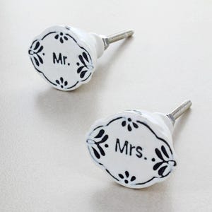 Può includere: Due pomelli per armadi in ceramica bianca con disegni floreali neri e le parole "Mr." e "Mrs.". I pomelli hanno una vite argentata per l'installazione. I pomelli sono un accento decorativo per mobili.