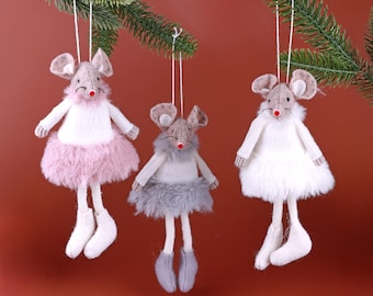 Op de afbeelding: Drie pluche muisornamenten met bungelende poten en witte touwhangers. Elke muis heeft een grijze kop, een rode neus en een fluffy rok in roze, grijs of wit. De ornamenten hangen aan een groene tak.