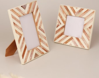 Op de afbeelding: Twee decoratieve fotolijsten. Eén is rechthoekig en de andere vierkant. Beide hebben een crèmekleurige achtergrond met een visgraatpatroon in bruintinten. De rechthoekige lijst heeft een bruine standaard.