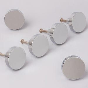 Könnte beinhalten: Sechs glänzende, verchromte Schrankknöpfe. Jeder Knopf hat eine runde Oberfläche und einen kleinen, goldfarbenen Stiel. Die Knöpfe sind auf hellem Hintergrund angeordnet, um ihre reflektierenden Oberflächen hervorzuheben. Geeignet für Möbel und Heimdekoration. Jeder Knopf hat einen Durchmesser von etwa 3 cm.