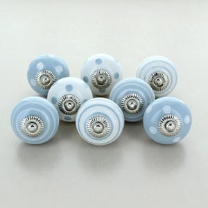 May include: Eight ceramic cabinet knobs in blue and white. Some knobs have a polka dot design, others have horizontal stripes. Each knob features a silver-coloured metal base.