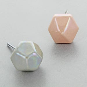 Può includere: Due pomelli geometrici per armadi. Uno è bianco perlescente, l'altro è di un colore pesca tenue. Entrambi hanno un design sfaccettato e una vite argentata per l'installazione. Questi pomelli decorativi aggiungono un tocco moderno ai mobili.