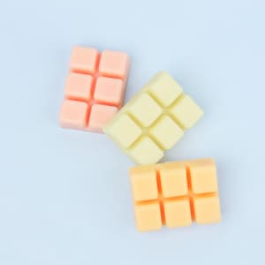 May include: Three wax melt bars in shades of peach, yellow, and orange. Each bar is divided into six squares. The wax melts are arranged on a light blue background. These are ideal for use in a wax warmer.